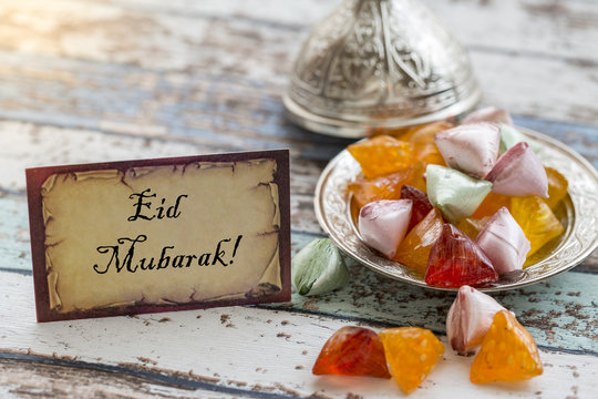 Eid mubarak text on greeting card on vintage table with candies on metallic plate