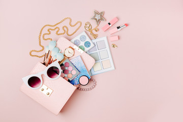 Cosmetic products flowing from Makeup bag on pastel pink background.  Flat lay, top view. Fashion concept