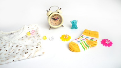 children's baby's undershirt, yellow socks, color crystals and asterisks, the alarm clock, a little blue bear cub on a white background. preparation for the birth of the kid