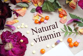 background from dry flowers and multi-colored pharmaceutical drugs, inscription Natural vitamin
