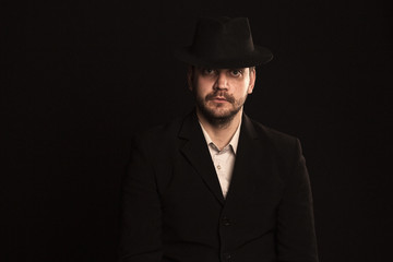 man in a classic suit and hat on a black background looks at the frame