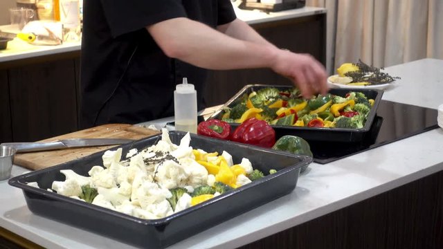 4K view of chef mixes vegetables for cooking. Broccoli, cauliflower and pepper marinated in a tray on the table.