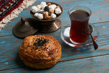 Gogal and glass of black tea with traditional snack in copper bowl, on rustic wooden table. Azerbaijan national Novruz holiday pastry 