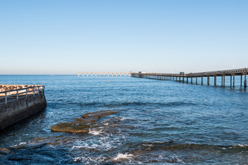 The Ocean Beach fishing pier in San Diego, California, with a rocky reef and sea wall in the foreground.