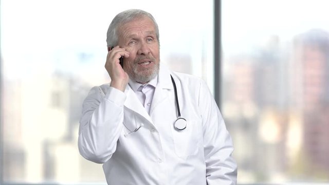Cheerful caucasian doctor talking on phone. Happy medical doctor talking on his cell phone on blurred background.