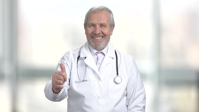 Senior doctor showing thumb up. Happy smiling male doctor gesturing thumb up on blurred background. Human emotions and gestures.