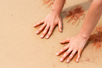 Woman hands creating shapes with red sand on the beach in aboriginal art style