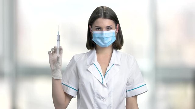 Portrait of young nurse holding syringe. Portrait of female doctor in lab coat and protective mask with a syringe. People, medicine, healthcare.