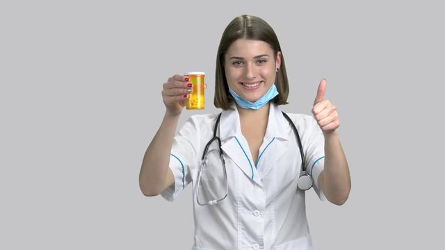 Doctor holding a bottle of prescription drugs. Beautiful caucasian doctor holding pills and giving humb up sign on gray background.