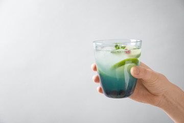 Woman holding glass of fresh lemonade on light background