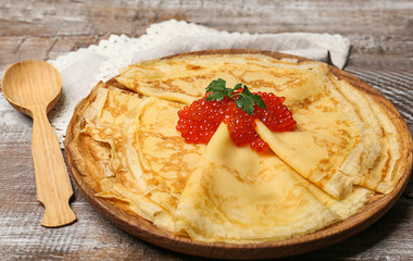Plate with thin pancakes and red caviar on wooden table, closeup