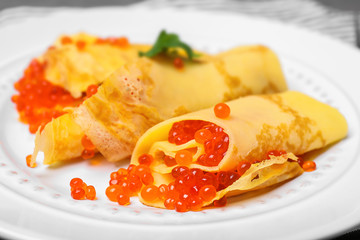 Thin pancakes with delicious red caviar on plate, closeup