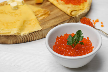 Bowl with delicious red caviar on white wooden table