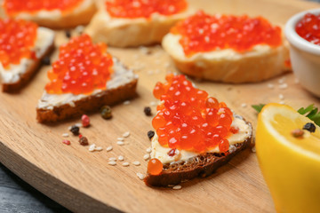 Tasty sandwiches with red caviar on wooden plate, closeup