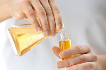 Woman pouring perfume oil into glass bottle, closeup