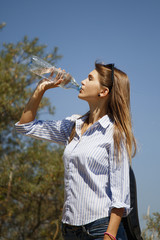 Healthy and sporty young woman drinking water from the bottle against green of summer forest