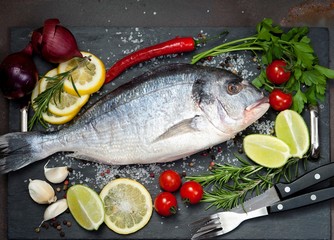 raw fish  Dorado  with spices and vegetables on slate plate