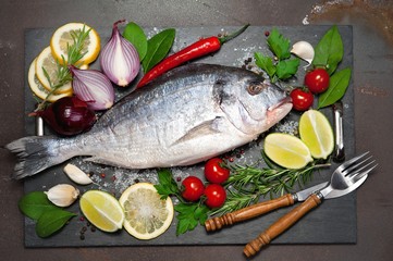 raw fish  Dorado  with spices and vegetables on slate plate