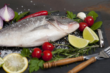 raw fish  Dorado  with spices and vegetables on slate plate