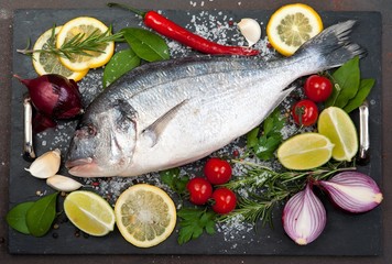 raw fish  Dorado  with spices and vegetables on slate plate