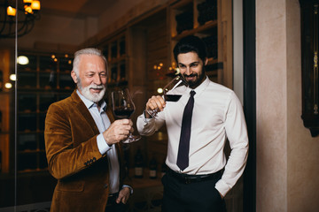 Winemakers in wine cellar holding glass of red wine and checking it. Sommeliers testing wines in winery.