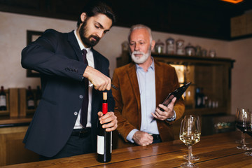 Winemakers in wine cellar holding glass of wine and checking it. Sommeliers testing wines in winery.