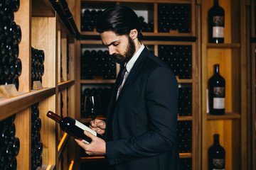Winemaker in wine cellar holding glass of red wine and checking it. 
