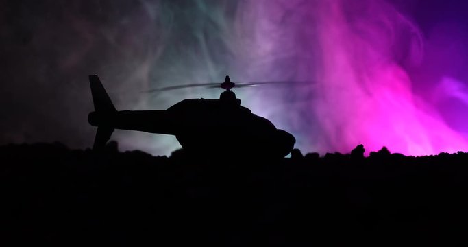 Slider shot. Silhouette of military helicopter ready to fly from conflict zone. Decorated night footage with helicopter starting in desert with foggy toned backlit. Selective focus. War concept
