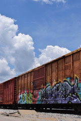 Old rusty train cars covered with graffiti on train track, with blue sky. 
