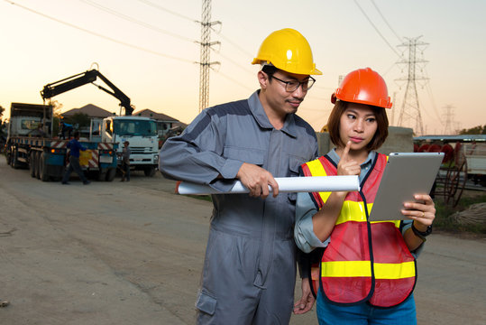 Electrical engineer and woman engineer are working together and holding blueprint and tablet at feild site work close to power electricity pole,