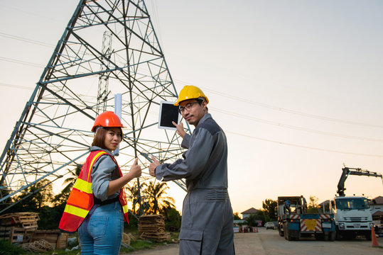 Electrical engineer and woman engineer are showing up thump and holding blueprint and tablet at feild site work close to power electricity pole, look at camera
