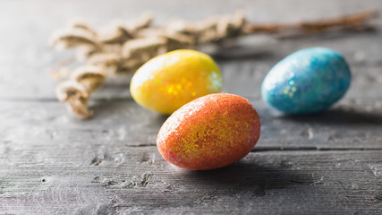 Three colorful eggs and a branch of willow on a dark wooden table. The decoration of the Easter table.