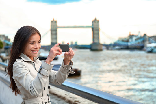 London woman tourist taking photo of Tower Bridge. London woman taking photos with mobile smart phone camera. Girl enjoying view over the River Thames, London, England, Great Britain. UK tourism.