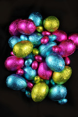 Pile of foil wrapped chocolate easter eggs in pink, blue & lime green.