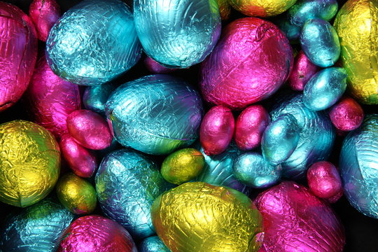 Pile of foil wrapped chocolate easter eggs in pink, blue & lime green.