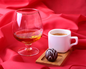 White cup of coffee and cognac in a glasses, pralines on red background.