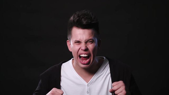 An attractive young man showing anger and shouts against a black background. Close-up Shot
