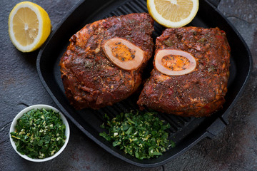 Cast-iron grill with raw marinated cross cut veal shank for making ossobuco with gremolata, selective focus, studio shot