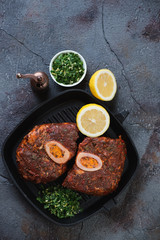 Uncooked marinated cross cut veal shank with gremolata, view from above on a cracked weathered asphalt background, vertical shot