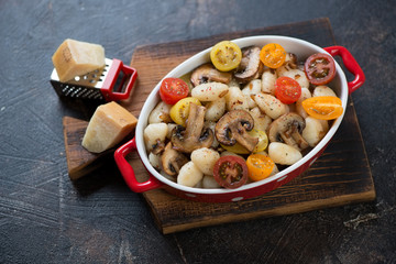 Potato gnocchi with fried champignons and fresh cherry tomatoes in a bowl on a rustic wooden serving board, horizontal shot
