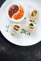 White plate with steamed meat dumplings manti, sauces and greens. View from above on a dark brown metal surface, vertical shot with copyspace