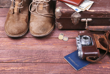 Travel concept with Vintage suitcase, sunglasses, old camera, suede boots, case for money and passport on wooden floor.