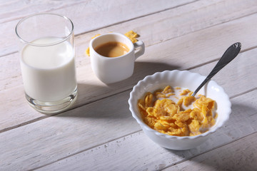 Corn Flakes cereal in a bowl, glass with milk and cap with espresso coffee. Morning breakfast.