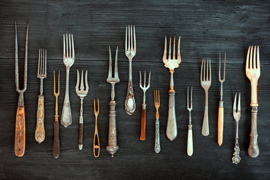 Top view on various forks, old utensils. Flat lay on rustic  dark wooden background. Antique kitchenware background