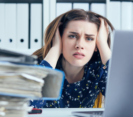 Tired and exhausted woman looks at the camera near mountain of documents propping up her head with...
