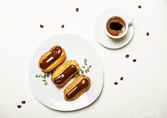 Eclairs cakes and morning espresso coffee in a cup, unhealthy breakfast, white background, top view