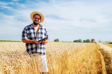 Smiling bearded man standing in the field on a sunny day and looking into a camera.