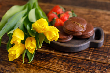 Fototapeta na wymiar Yellow tulips, biscuits and strawberries on a wooden table. A nice gift for your beloved. A bouquet of tulips and a treat.