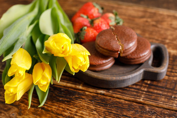A gift for Valentine's Day. Romantic treat. Yellow tulips, biscuits and strawberries on a wooden table. A nice gift for your beloved.