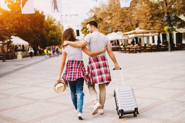 Rear view of attractive man with travelling bag walking with cute girl with a hat and hugging.